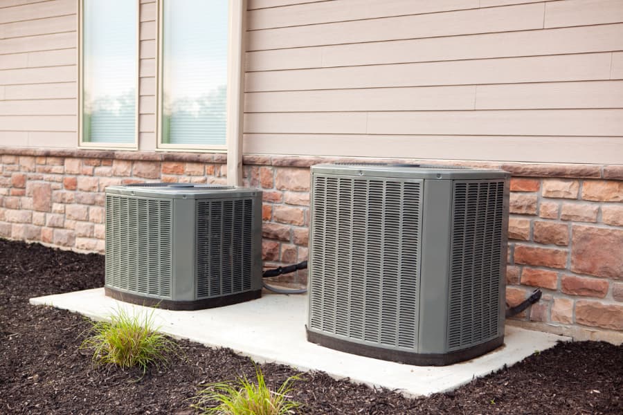 2 HVAC units side by side next to a beige house