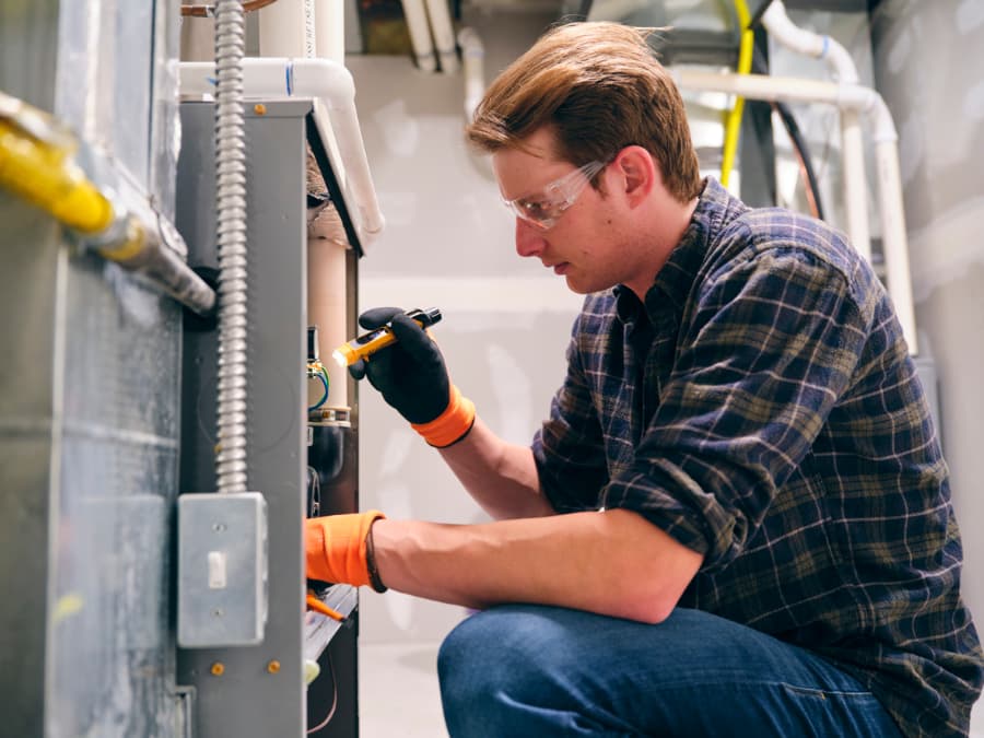 Repair worker inspecting furnace inside home with flashlight