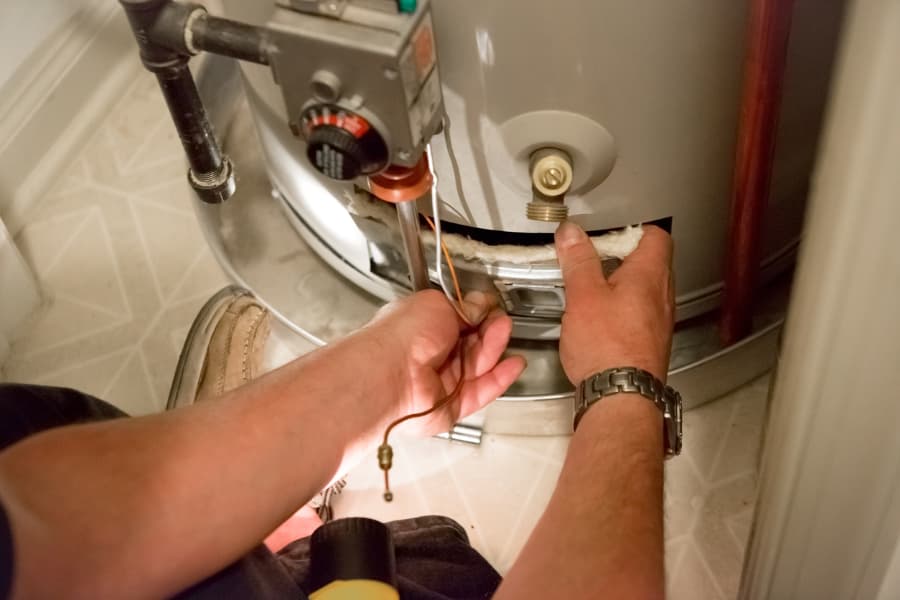 repairman shines a flashlight on a hot water heater 