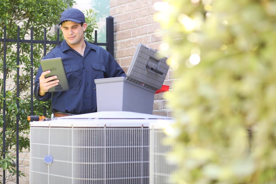 Service technician measures performance of unit outside of home for central air conditioner winter maintenance  