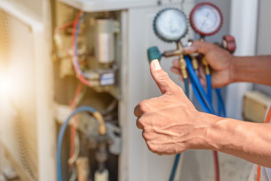 tech using a gauge and giving a thumbs up on an AC repair