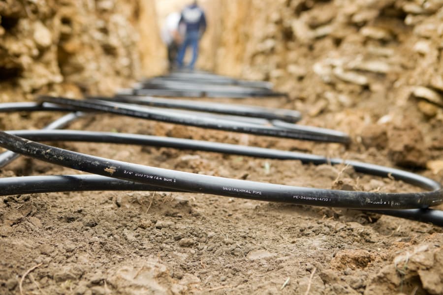 worker laying geothermal coils in trench